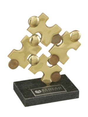 Estatueta de metal dourado representando peças de quebra-cabeça interligadas sobre uma base de mármore.